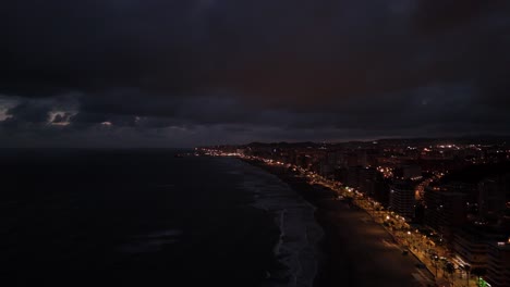 aerial view of torreblanca, spain coastline at night showing illuminated buildings, dark sea, and cloudy sky, creating a dramatic and moody atmosphere, drone pulling out