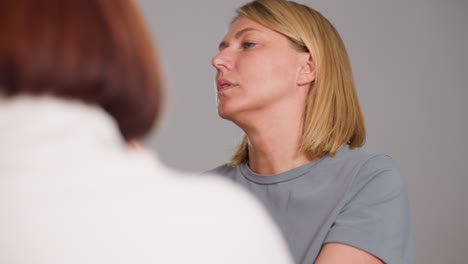 seamstress in grey tee carefully adjusts dress neckline while discussing fit details with colleague backing camera, exchanging insights, ensuring smooth finish during collaborative studio session