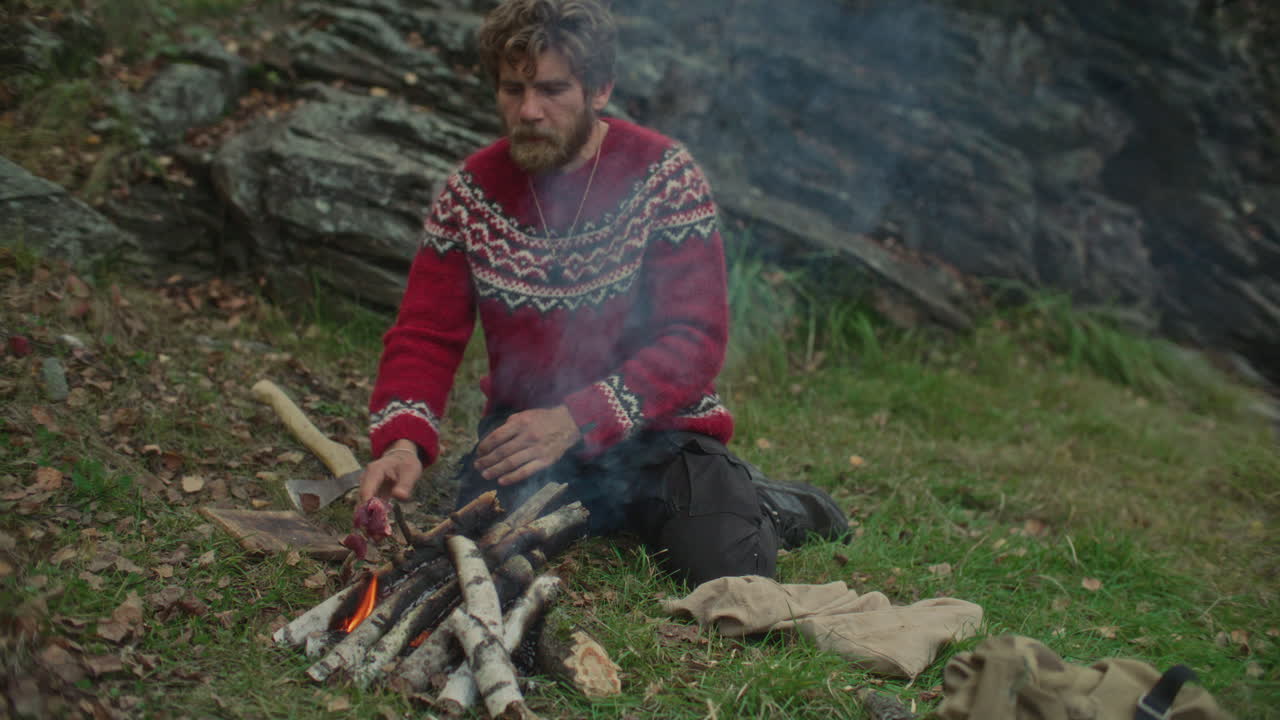 Man Cooking Meat on Sticks over Campfire during Survival Trip in Nature