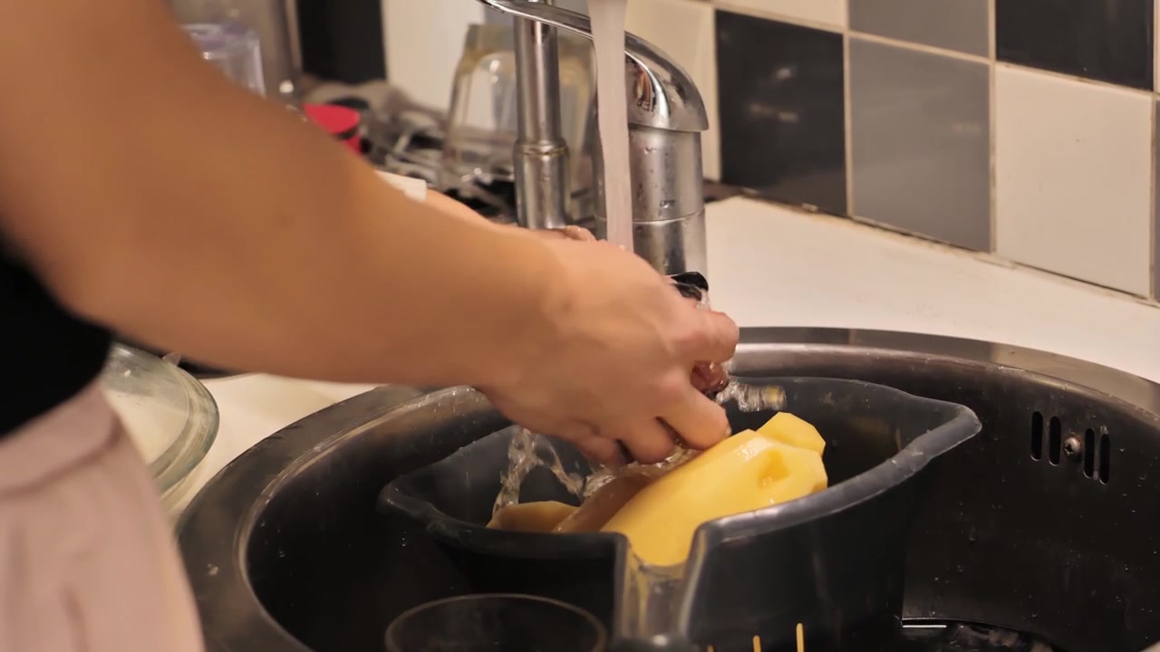Primer plano de una mujer lavando patatas peladas bajo un grifo abierto en el fregadero 4K.