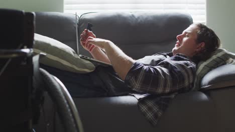 happy caucasian disabled man lying on sofa in living room using laptop