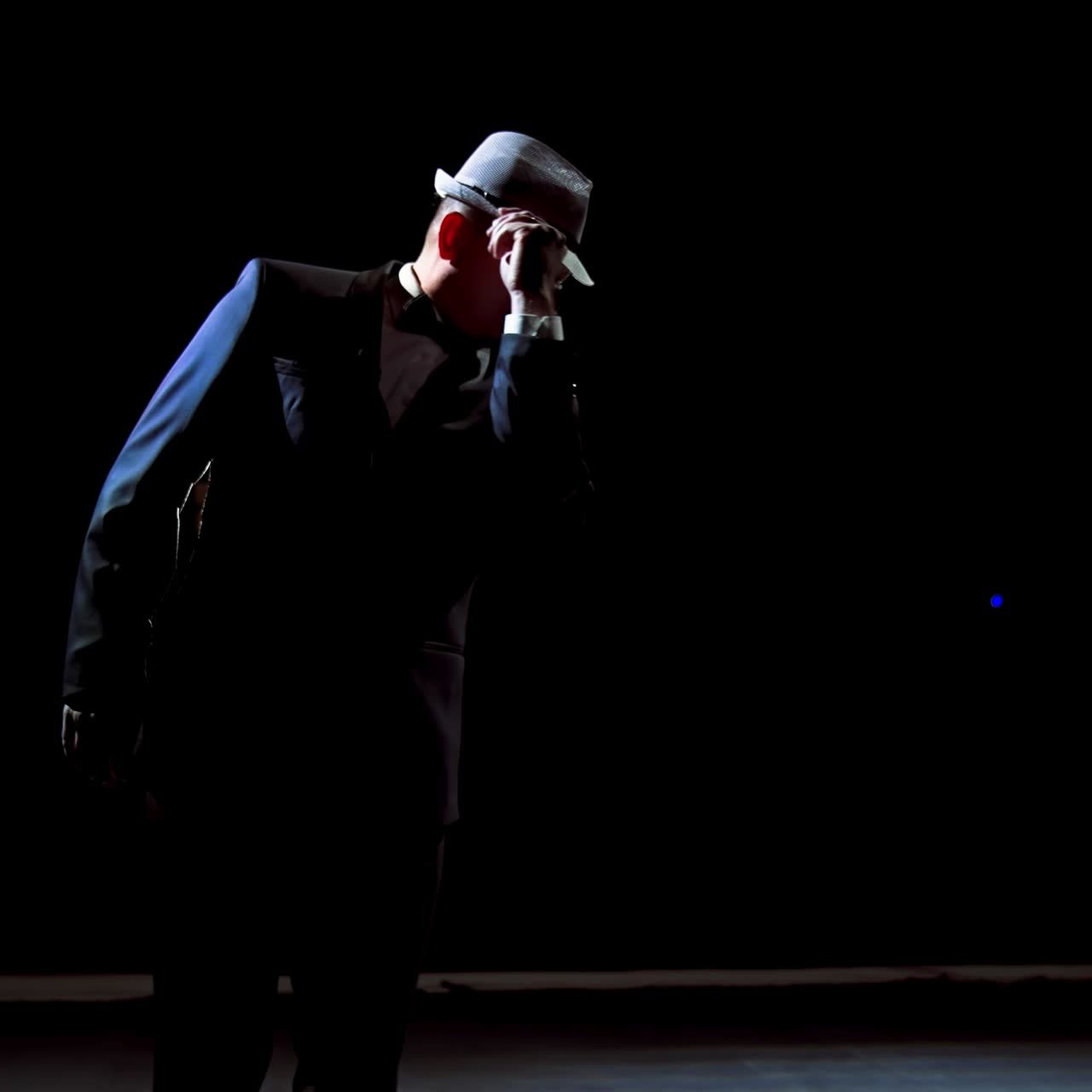 Actor man on a stage. Dark silhouette of a man wearing suit performing on a scene in theatre at spotlight. View from the stage