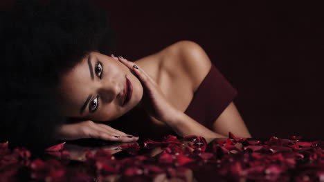 Retrato-Hermosa-Mujer-Afroamericana-Relajante-Pétalos-De-Rosa-Cayendo-Sobre-La-Piel-Suave-Mujer-Sensual-Soñando-Con-Un-Romance-De-Fantasía-íntima-Que-Complace-El-Deseo-En-El-Concepto-Del-Día-De-San-Valentín-Rojo