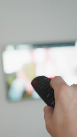 mano sosteniendo el control remoto delante de la tv, árbol de navidad en borrón, tiro de pov