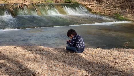 Junge-Spielt-Mit-Steinen-Am-Ufer-Des-Flusses