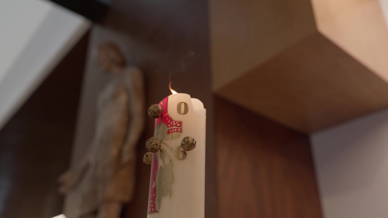 Vela de pilar blanca atada con una cinta roja y capullos secos de pie en un interior cálido.