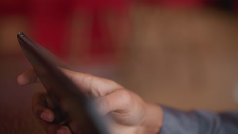 immigrant holding tablet with fingertips in soft light, close-up view of hand gripping edge of device, captured indoors with blurred background, relaxation, and digital engagement in modern setting