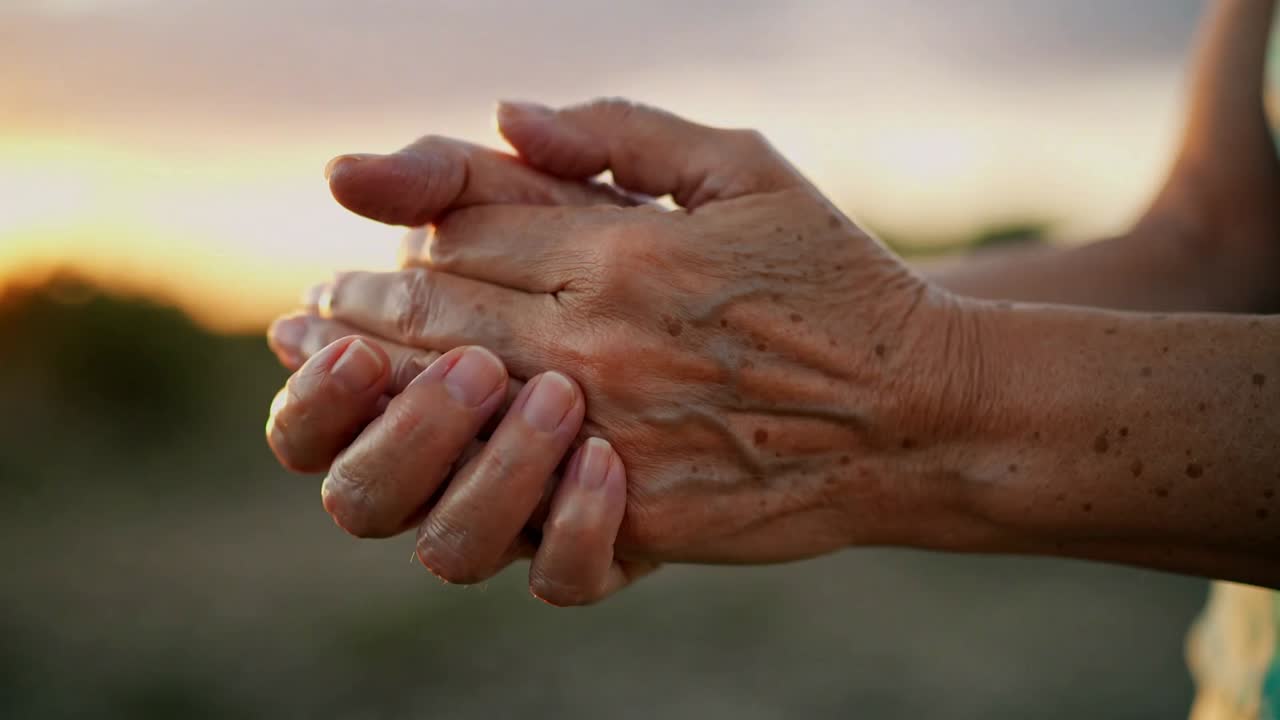 Bringing senior hands together, fingers shifting and thumbs pressing at sunset, adjusting grip
