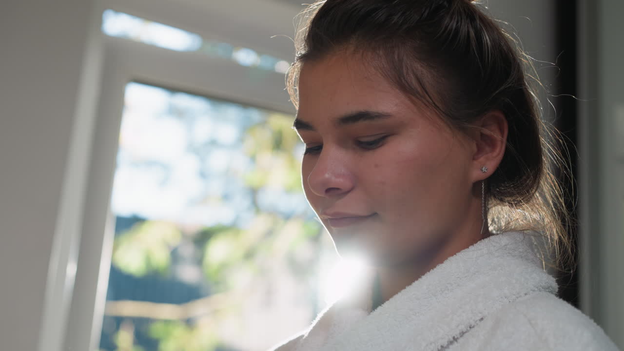una mujer cocina en la cocina por la mañana en primer plano. una mujer bonita con un acogedor y esponjoso manto de baño está de pie junto a la ventana a la luz del sol.
