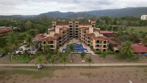 Aerial-footage-of-the-beach-on-a-sunny-day,-from-a-hotel-with-a-pool-in-Costa-Rica,-Aerial-drone-footage,-Jaco-Beach,-Puntarenas,-Costa-Rica,-Pull-Back