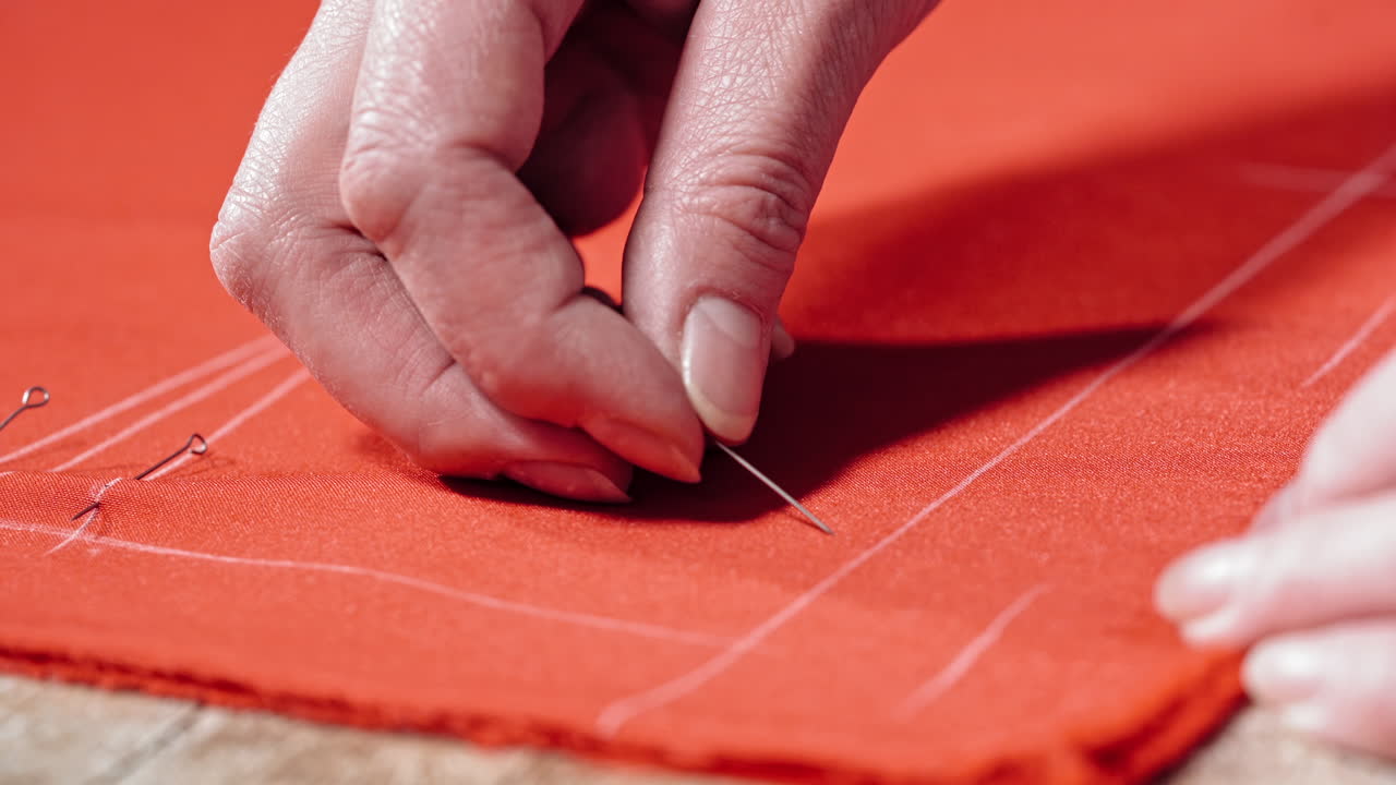 Female hands of the skilled worker putting the pin to the fabric. Red cloth with white lines and a tailor pinning the material on the table. Concept sewing and handicraft.