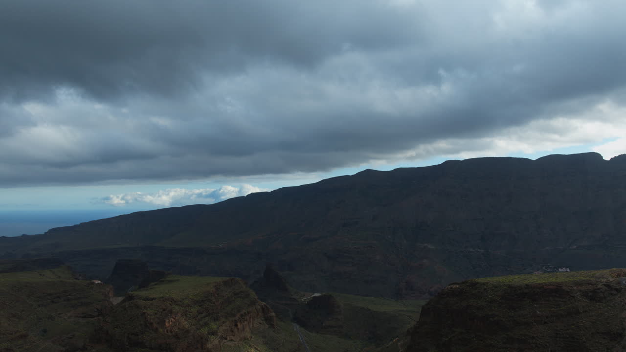 Billowing white clouds drifting slowly across rugged mountain peaks in scenic Gran canaria landscape, revealing dramatic geological formations under bright daylight