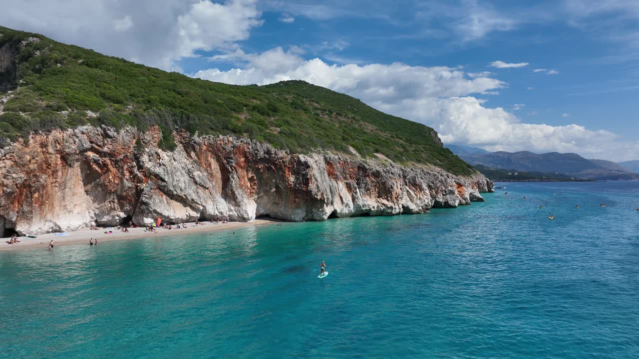 Expansive panoramic view of Gjipe Beach in Albania on a bright, sunny day. Focus on the beach, the cliffs, the turquoise water, and the overall scenic beauty.