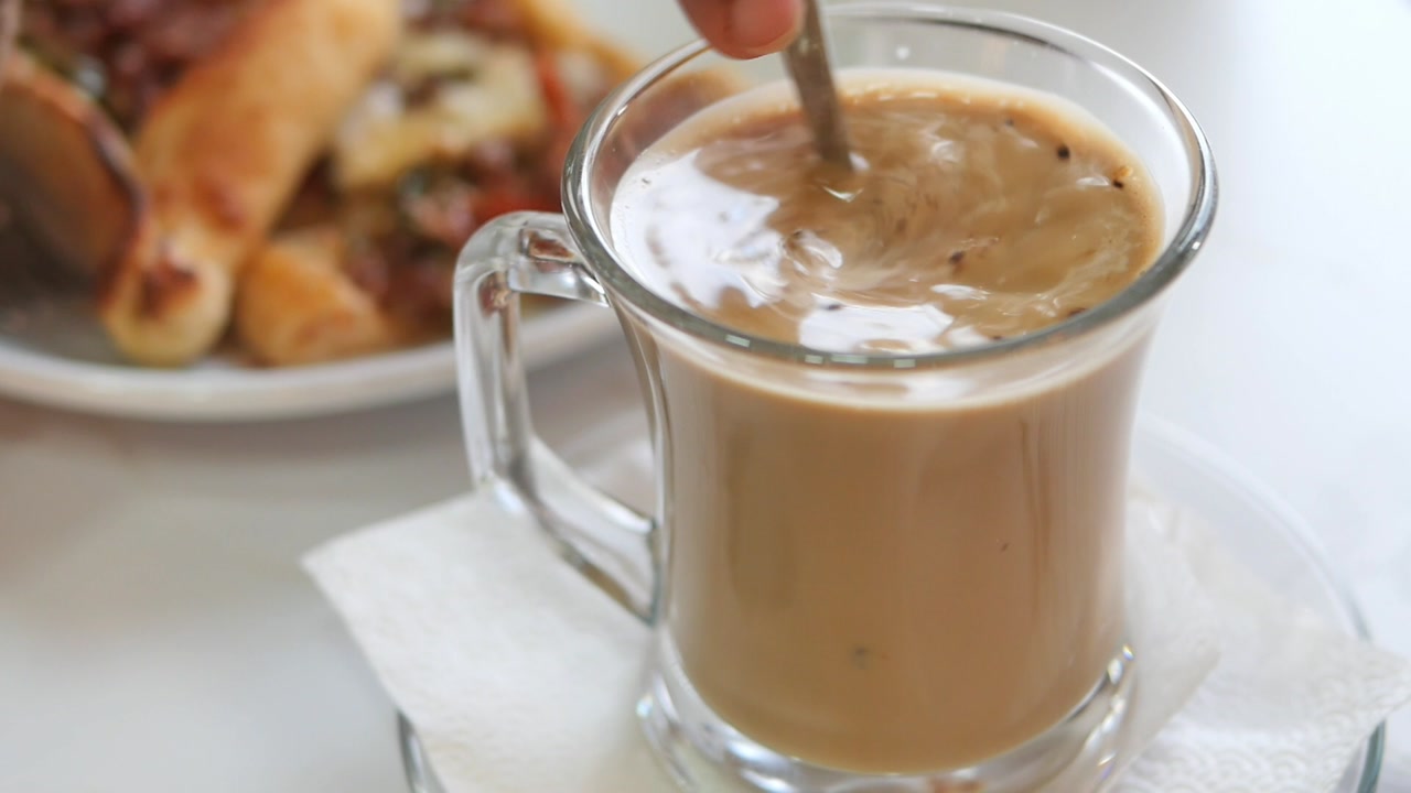 Person Stirring Creamy Coffee in a Glass Mug