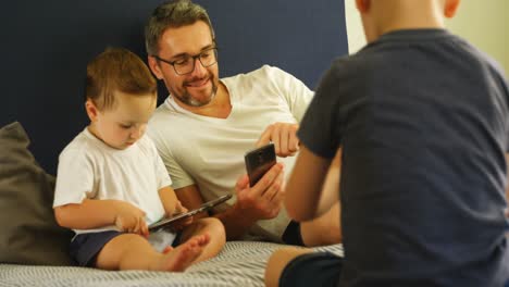 father and kids using mobile phone and digital tablet on bed 4k