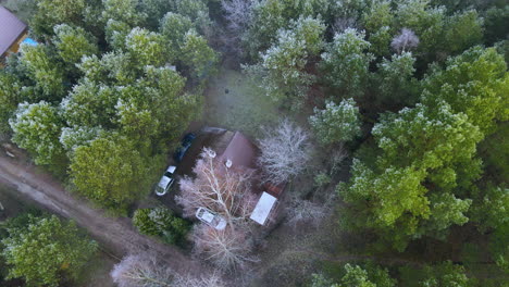 Vista-De-Una-Casa-De-Madera-Con-2-Autos-Rodeada-De-árboles-Verdes-En-Bartoszylas,-Polonia---Toma-Aérea