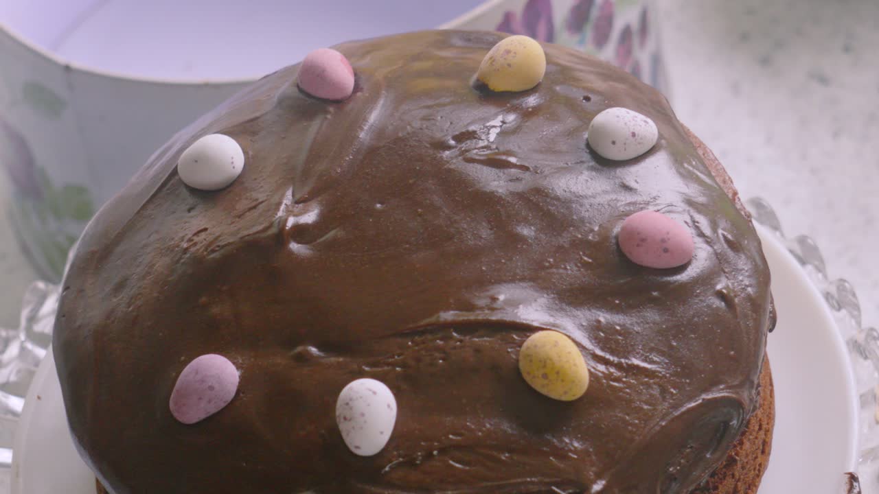 Overview of Easter Themed Chocolate Sponge Cake with Small Eggs on Top with Creamy Frosting Icing. Slow Motion Baking Food Footage.