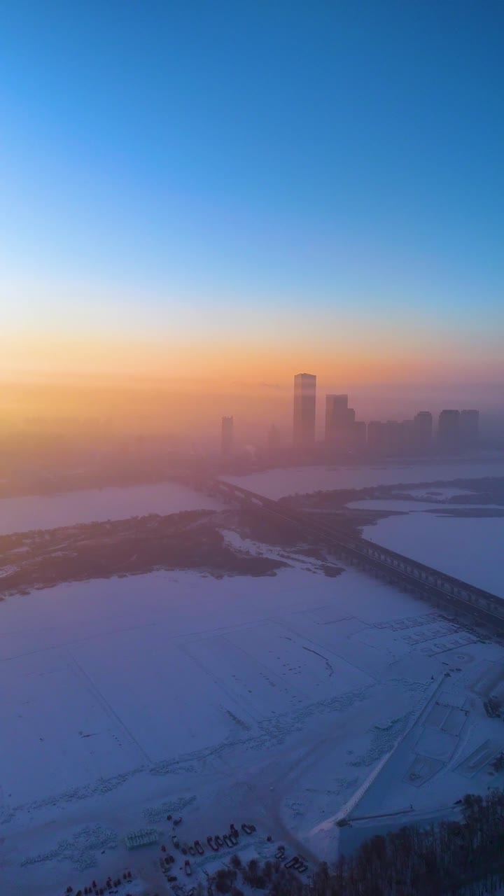 Vertical aerial drone shot of the Harbin City skyline with the frozen Songhua River at sunrise, China