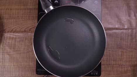 el nido, philippines - pouring a little amount of cooking oil to a hot black pan over the induction cooker - closeup shot