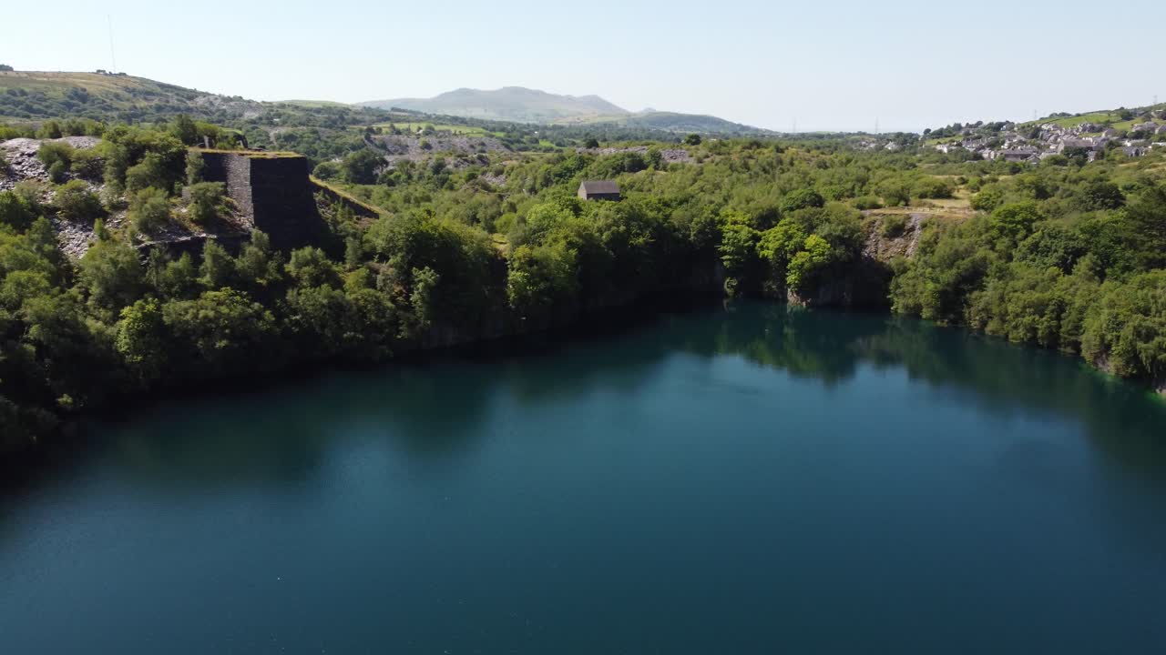 Vista aerea in discesa di una valle boscosa gallese con pozzo di estrazione dell'ardesia e lago della cava sotto le montagne della Snowdonia.