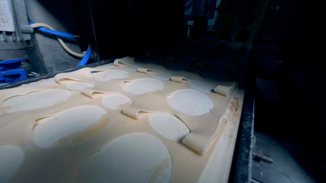 Remains of dough for pelmeni are falling into a plastic box.