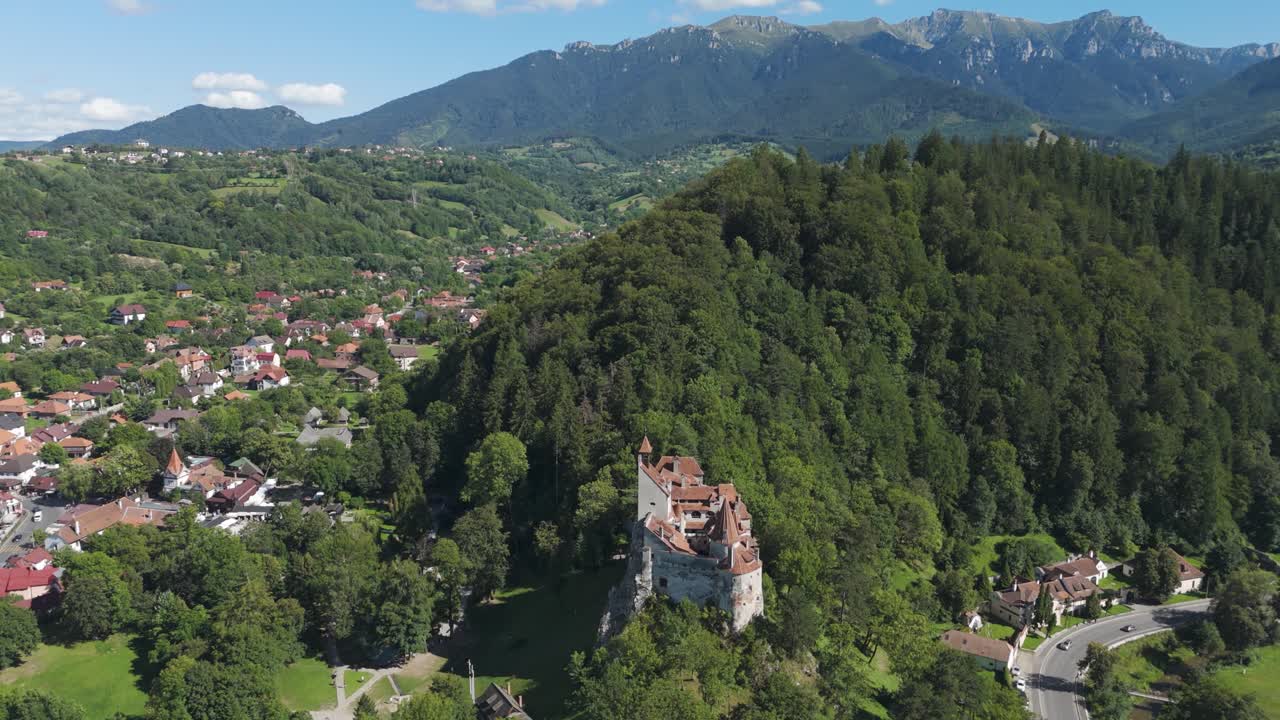 Drone orbit around Bran Castle with lush green hills providing a scenic natural backdrop