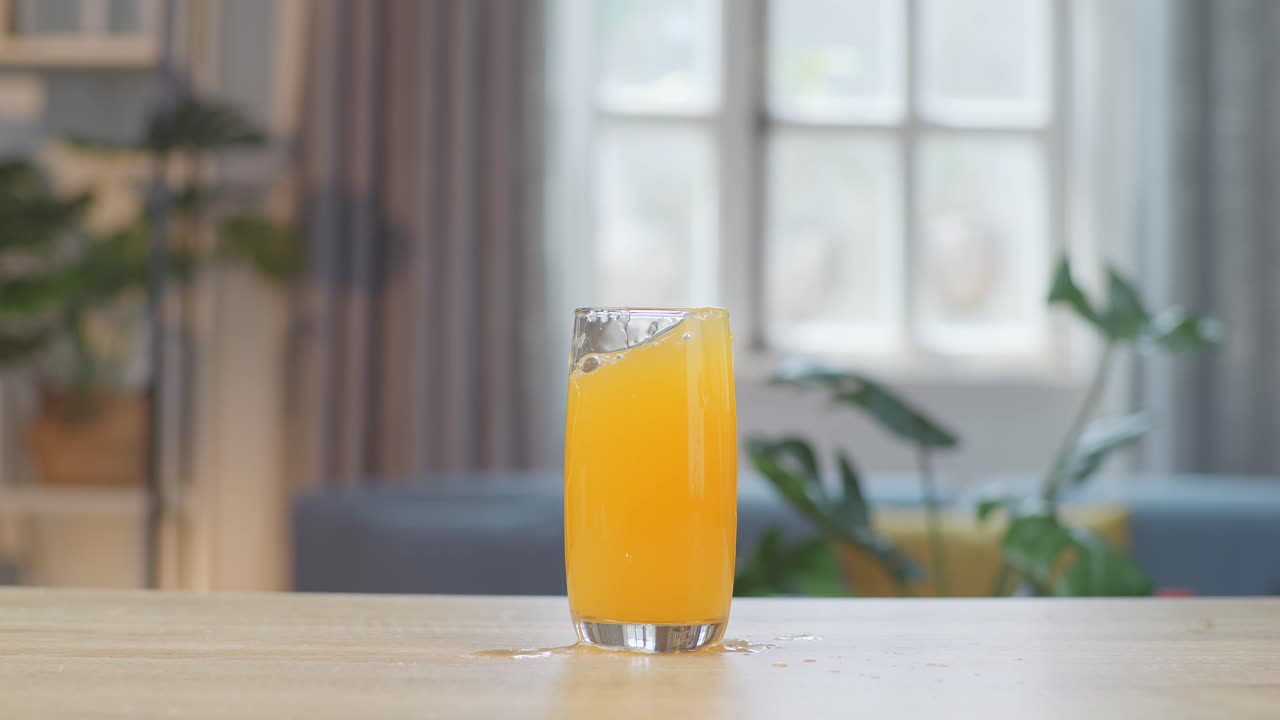 Cubetti di ghiaccio che cadono in un bicchiere di succo d'arancia sul tavolo di casa