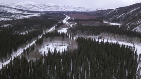 aerial tilt up view over alaska wilderness, snow covered hills in the background, frozen river and pond