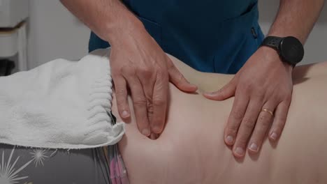 close up of a person pressing two fingers into a woman's lower back during a massage