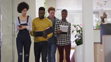 diverse smiling male and female business colleagues walking and discussing paperwork in office