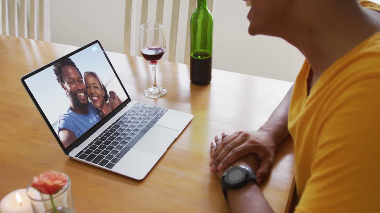 Mixed race man sitting at table using laptop making video call with friends