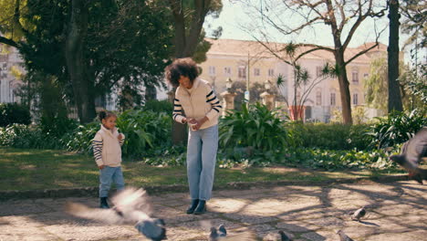 child feeding birds with mother in park. girl throwing food to pigeons.