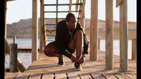 Afroamerikanischer-Männlicher-Jogger,-Der-Schnürsenkel-Am-Pier-Am-Strand-Bindet-4k