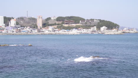 sea waves hitting onto a small rock with a view of a small port at the background (shoot info: cin2, 1080p, 59.94fps)