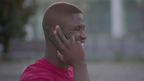primer plano de un hombre afroamericano hablando por teléfono en el parque, sonriendo
