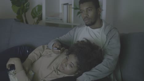joven pareja afroamericana escogiendo una película con el control remoto y comiendo palomitas de maíz en la oscuridad