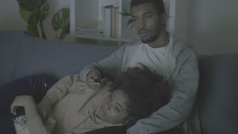 young african american couple picking a movie with the remote control and eating popcorn in the dark