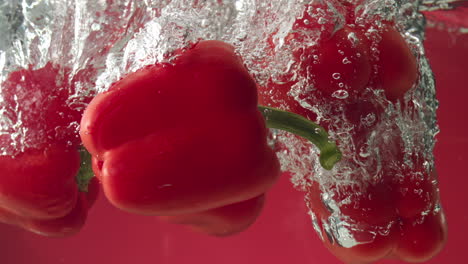 cámara lenta de pimientos rojos cayendo al agua sobre fondo rojo