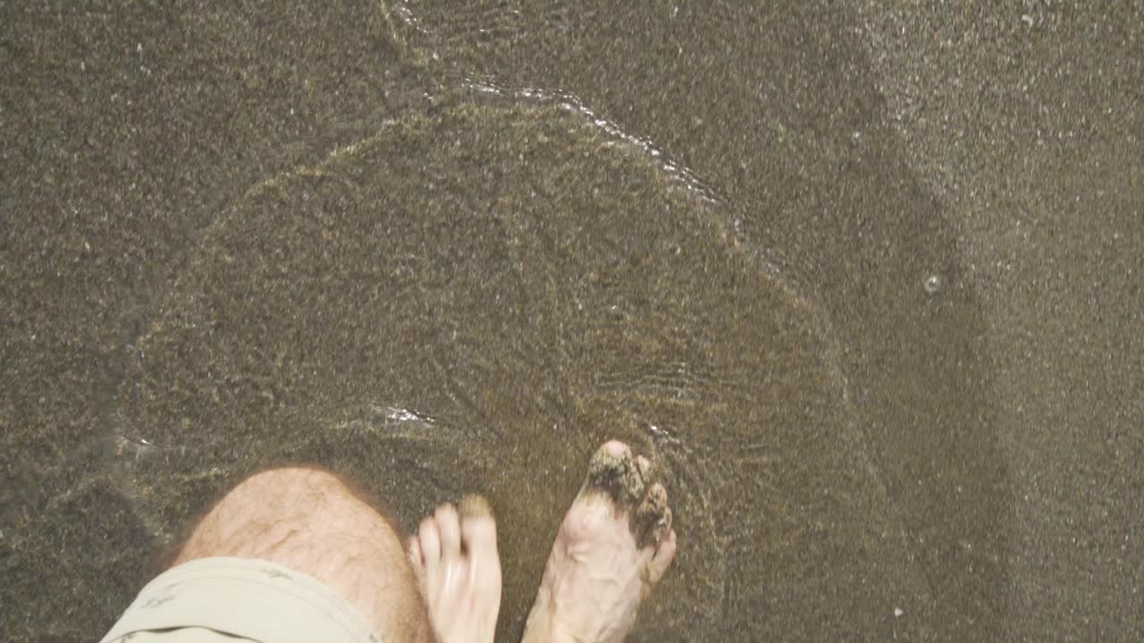 Male walking bear foot in the wet sand on the Beach at Cala de Mijas on the Costa Del Sol in Southern Spain as the surf gently washes in and out.