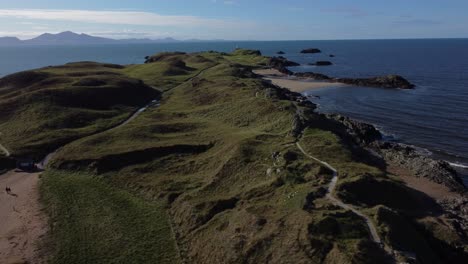 vista aérea en órbita de ynys llanddwyn, isla galesa con el océano reluciente y la niebla de la cordillera de snowdonia a través del horizonte del amanecer.
