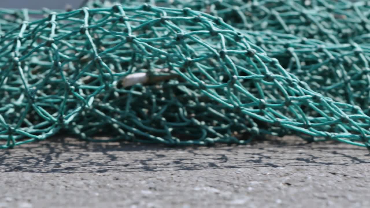 Spostando una rete da pesca verde intrecciata si rivela una clip d'argento su terreno pavimentato, la fotocamera si regola per un primo piano.