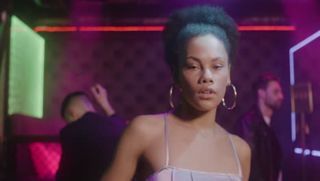 portrait of beautiful girl looking confident at camera at disco while her friends dancing behind her 2