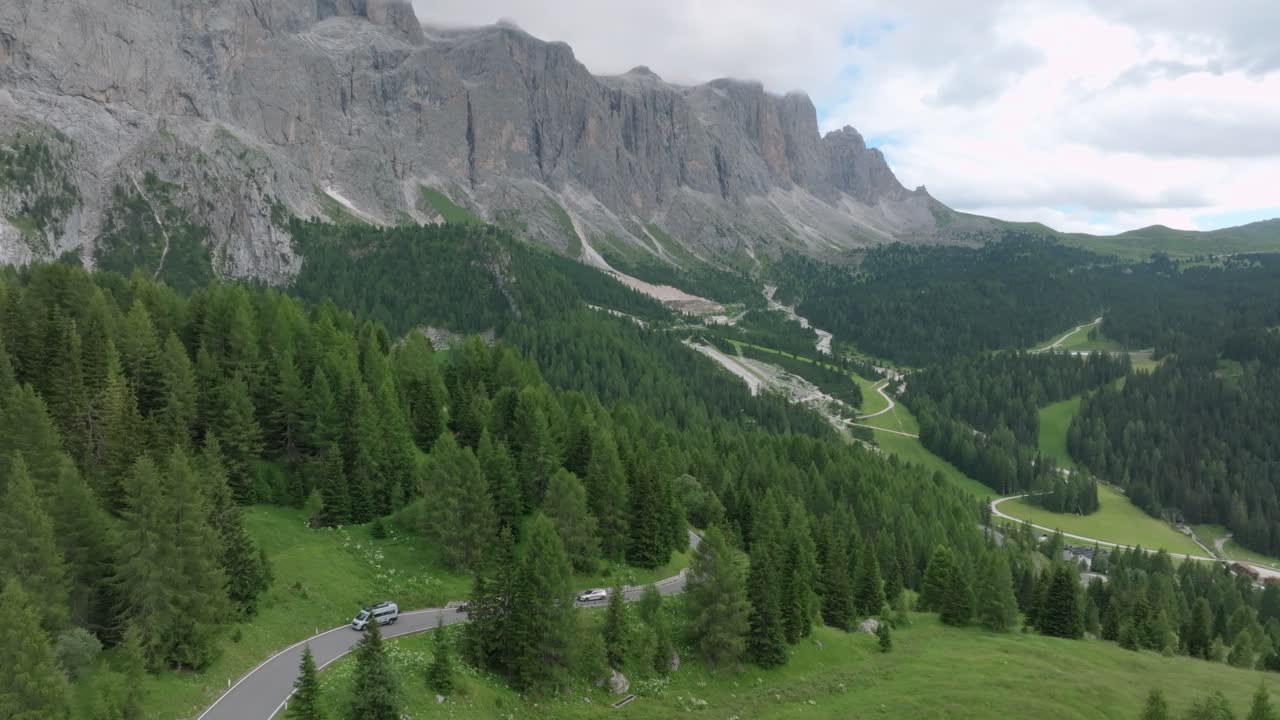 una toma aérea de un avión no tripulado captura varios coches serpenteando a lo largo de las carreteras cerca del paso de selva en las montañas dolomitas, trentino, tirol del sur, italia