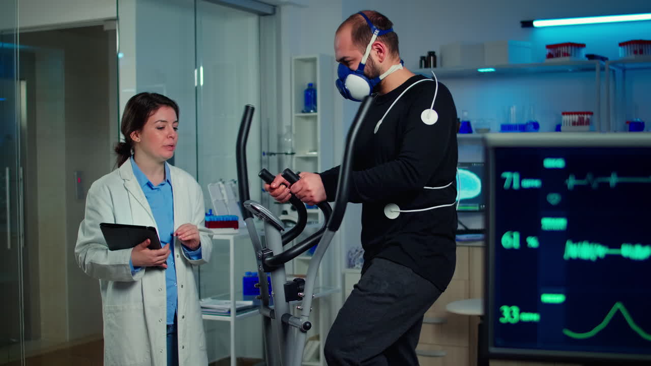 성능 운동 선수가 의학 연구원과 이야기하고 크로스 트레이너에서 달리고 있습니다.