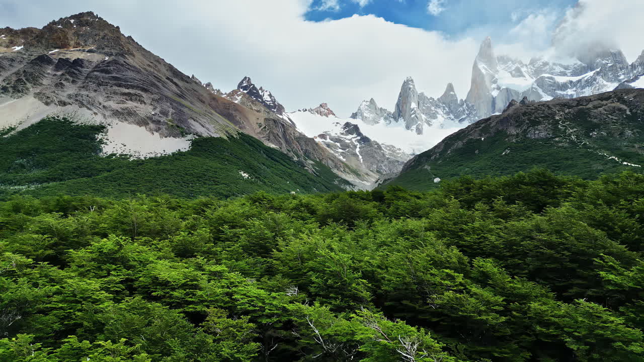 Vista aerea da drone sopra la lussureggiante foresta verde verso le imponenti cime del Fitz Roy coperte di neve e nuvole