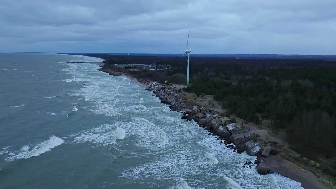 Starker Wind treibt die Turbine an, während dunkle Wellen in der Winterdämmerung an einer felsigen Küste brechen