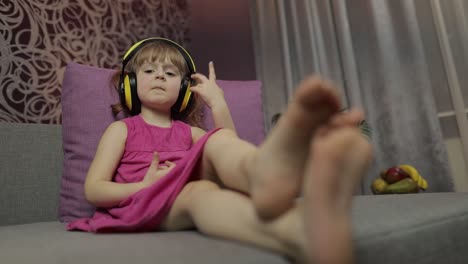 Little-child-girl-in-headphones-enjoying-listen-music.-Dancing-on-sofa-at-home