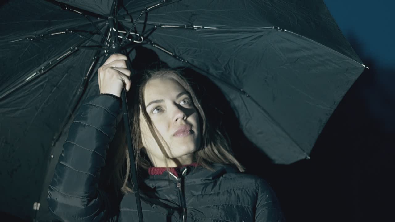 una donna sorridente tiene un ombrello sotto la pioggia notturna in slow motion