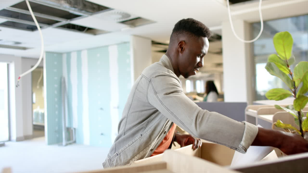 Casual african american businessman carrying box moving into office, slow motion with copy space