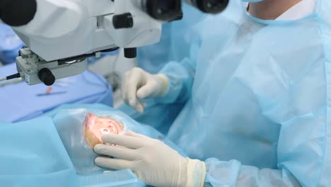 ophthalmological surgery specialist sits in front of microscope performing operation. low angle view on the female doctor conducting high-precision surgery. femto laser assisted cataract surgery.